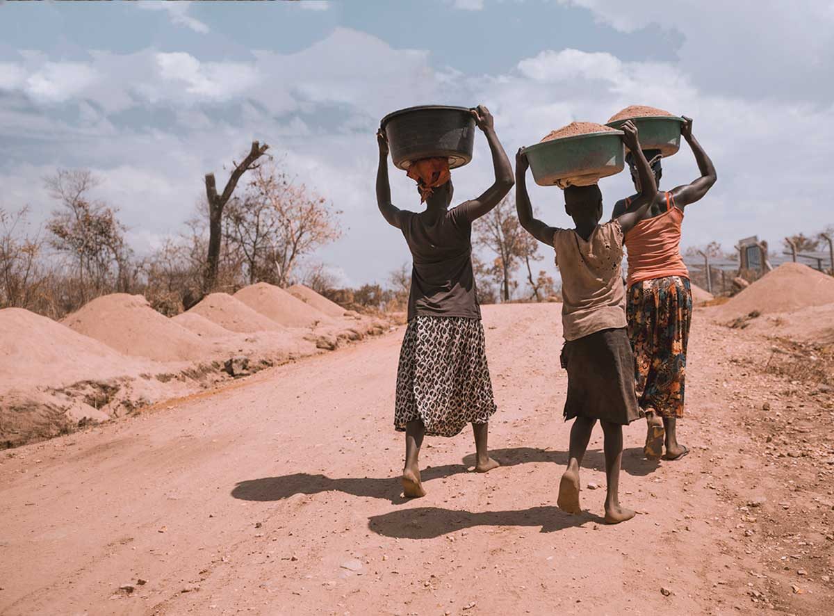 Women carrying basins on their heads along a dirt road